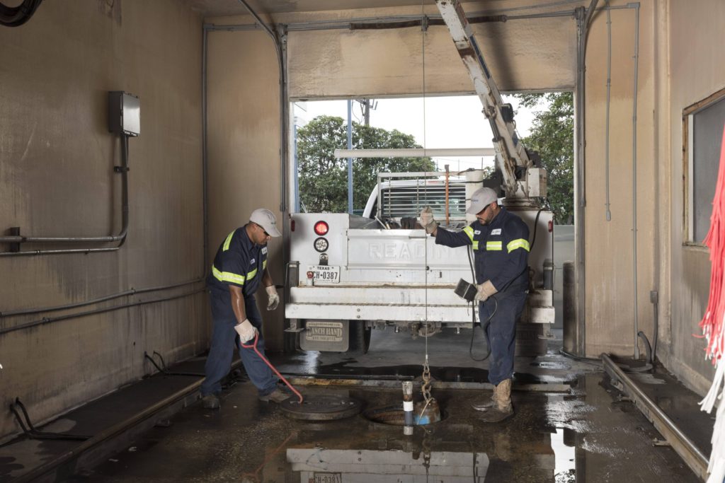 two silver city reps working on a grit trap in a car wash